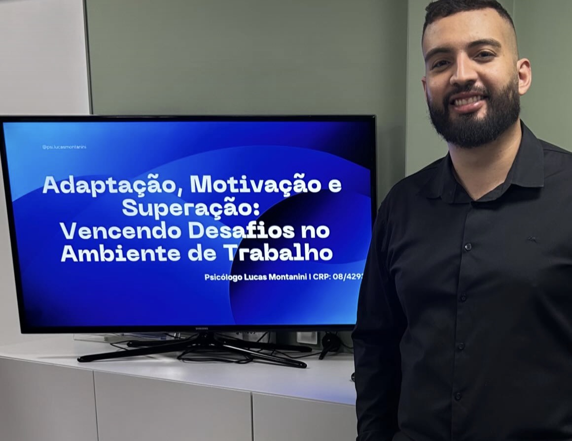 Lucas Montanini ao lado da tela da palestra Adaptação, motivação e superação